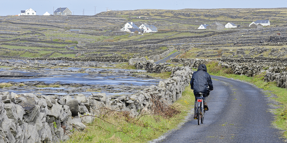 Cycliste sur la route, entre les champs lilliputiens cloisonnés de murets de pierre calcaire karstite, sur Inishmaan.